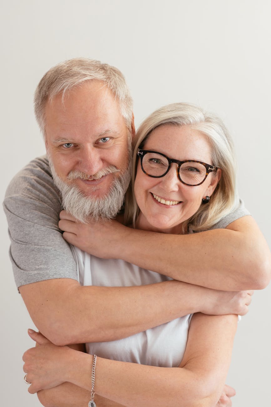 close up shot of a happy elderly couple hugging while looking at camera